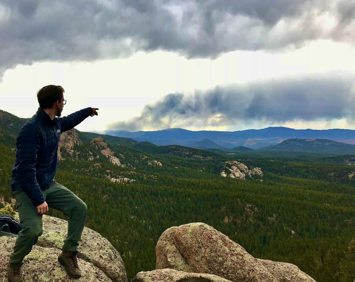 Roberto on a Colorado mountaintop, pointing toward distant clouds