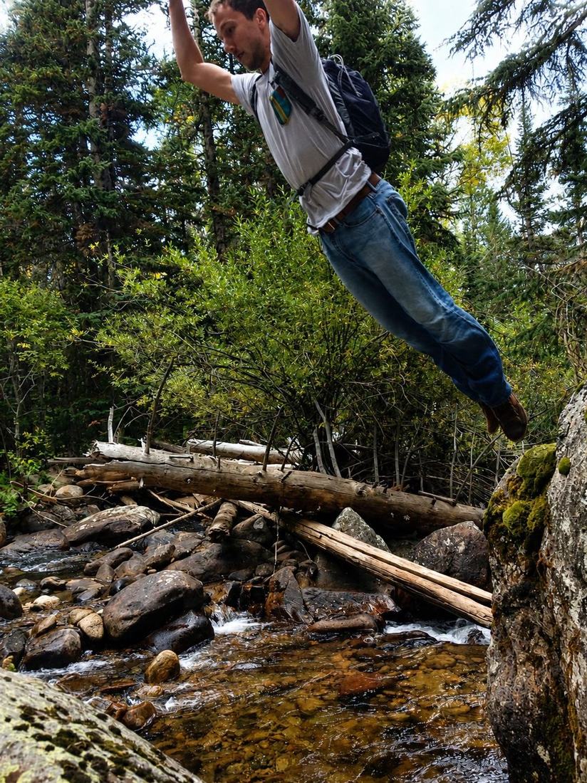 Roberto mid-leap across rocks over a forest stream